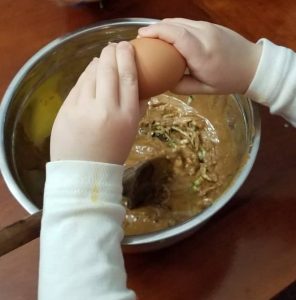 little kid hands breaking egg over bowl. Curbing the constant snacking by getting your kids in the ktichen