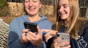 Two teenage girls laughing while looking at their cell phones.- kids' screen time