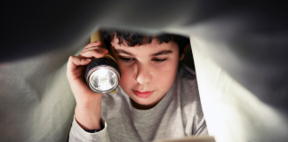 Young reader holding a flashlight and reading a story for book lovers under the covers.