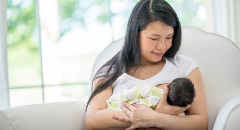 woman smiling and breastfeeding her newborn in a bright room