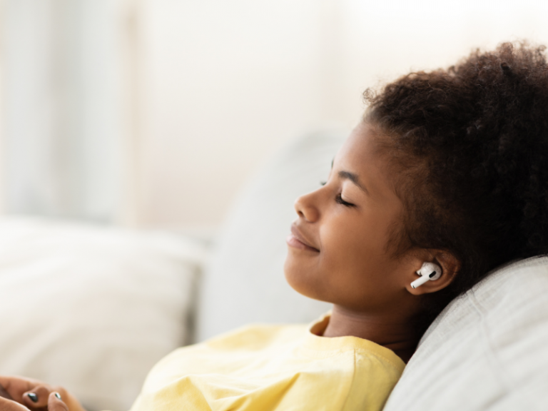 Teen rests on couch with earbuds in and eyes closed, practicing progressive muscle relaxation