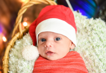 Newborn baby, swaddled, wearing a Santa hat in a basket