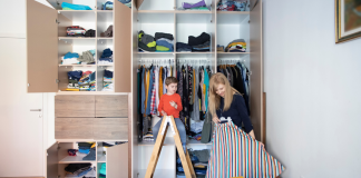 Mom with young son near large closet. They are organizing the closet together. Young son is on step ladder looking at Mom who is holding a skirt.