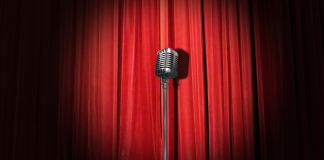 An old-fashioned microphone stands in front of a red curtain