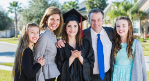 A family posing for a photo including mom, dad, two younger girls and a young woman in a cap and gown, celebrating the graduate