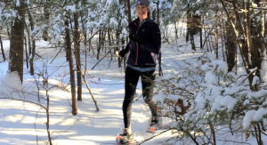 Woman snowshoeing through snow-covered woods on a sunny day.